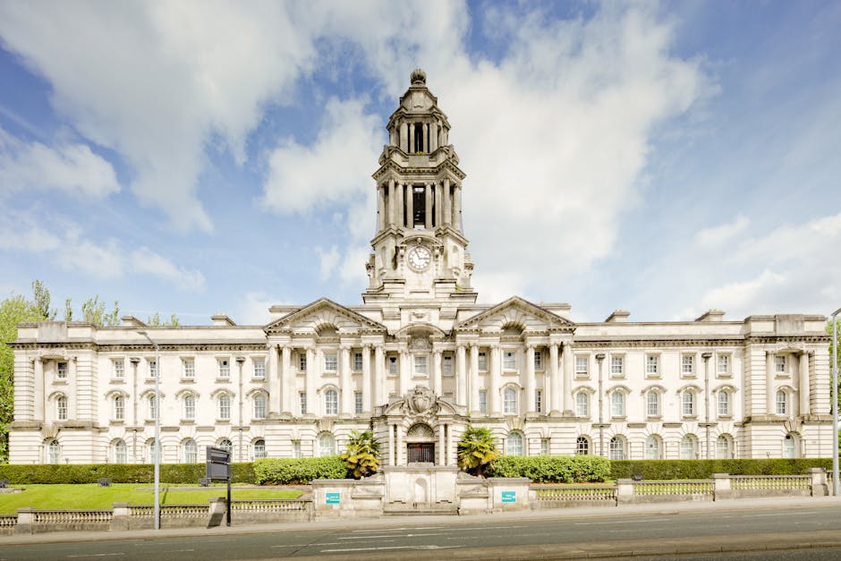 A large historic white stone building with architectural details including columns and decorative carvings, featuring a prominent clock tower at its center with a domed top and intricate detailing. Th