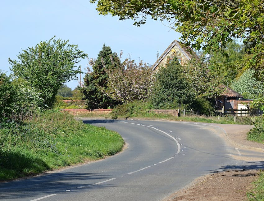 Photograph of a narrow rural lane in Cudham, with a stone cottage on the right side featuring a red British telephone booth situated near a 30 mph speed limit sign. The road is partially shaded by gre