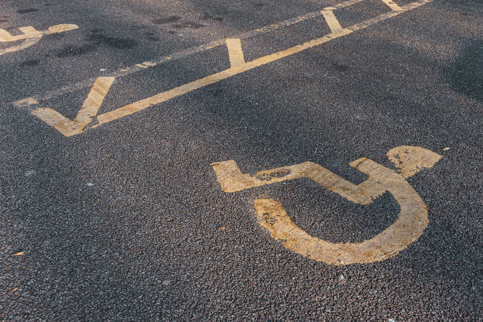 Close-up view of a designated accessible parking space on an asphalt driveway, featuring a yellow painted wheelchair symbol and diagonal striped lines, indicating it is reserved for individuals with m