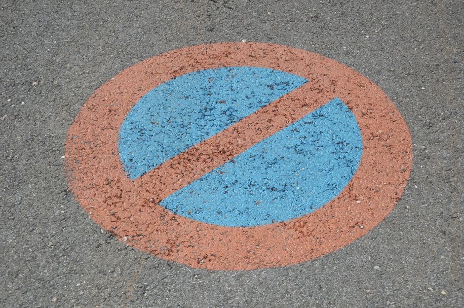 Close-up view of a designated accessible parking space on an asphalt driveway, featuring a yellow painted wheelchair symbol and diagonal striped lines, indicating it is reserved for individuals with m